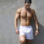 Muscular male bodybuilder standing against wall outdoors